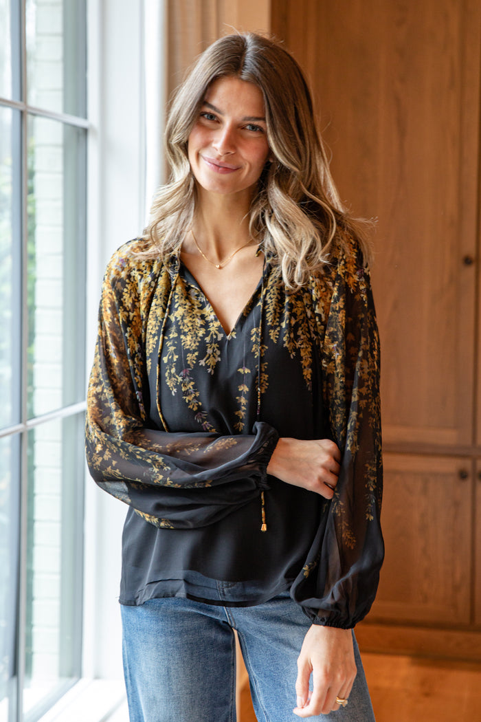 Woman wearing a floral blouse and jeans standing indoors.