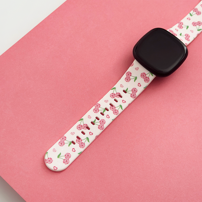 Coconut Lane Fitbit strap with cherry pattern and pink accents on a pink surface.