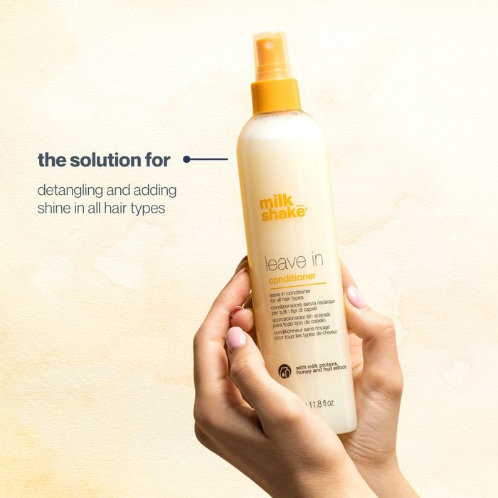 Hand holding a bottle of milk_shake  leave-in conditioner against a light background