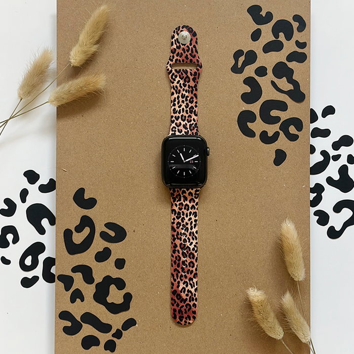 Brown Apple Watch strap with black leopard print, shown against a background of dried grass.