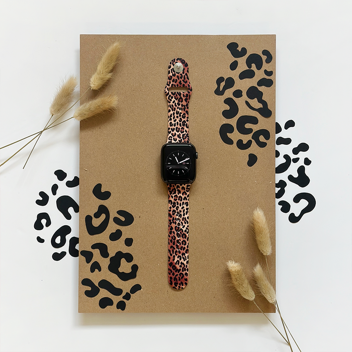 Coconut Lane Leopard Apple Watch strap with black animal spots, shown against a backdrop of dried grasses.