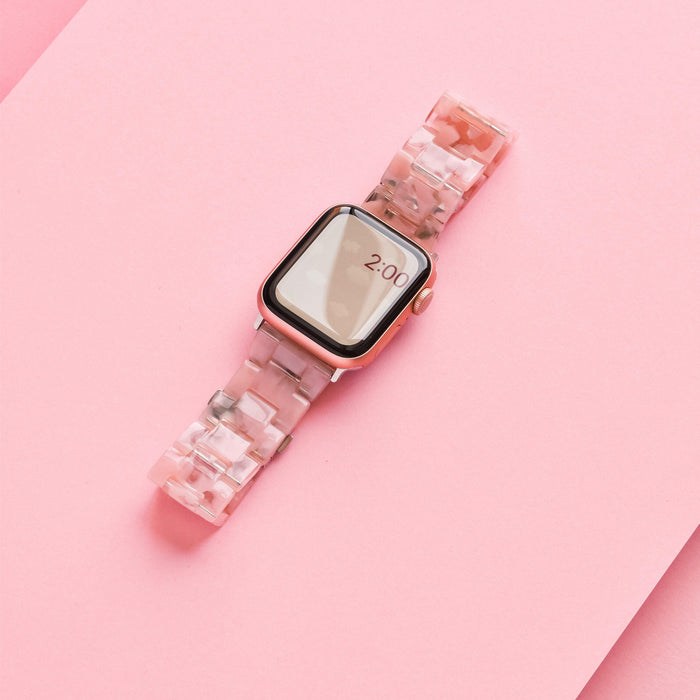 A girly and cute smartwatch with a rectangular face and rose gold casing is displayed on a pink background. The Luxe Pink Clouds Apple Watch Strap by Coconut Lane features a pink and white marbled pattern made of durable resin. The screen shows the time as 2:00.
