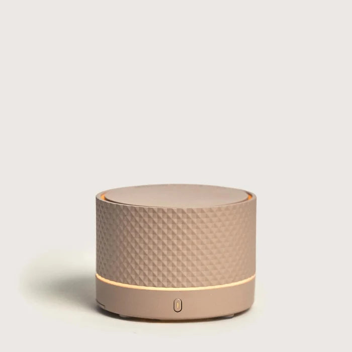 Round beige portable diffuser with textured surface on a light gray background
