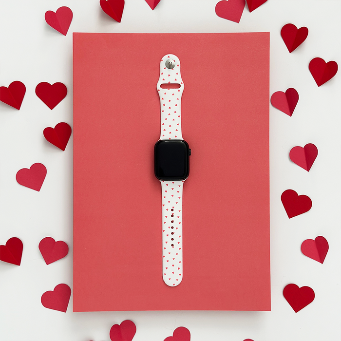 Coconut Lane Mini Hearts Apple Watch strap with heart pattern, shown on red paper scattered with red hearts.
