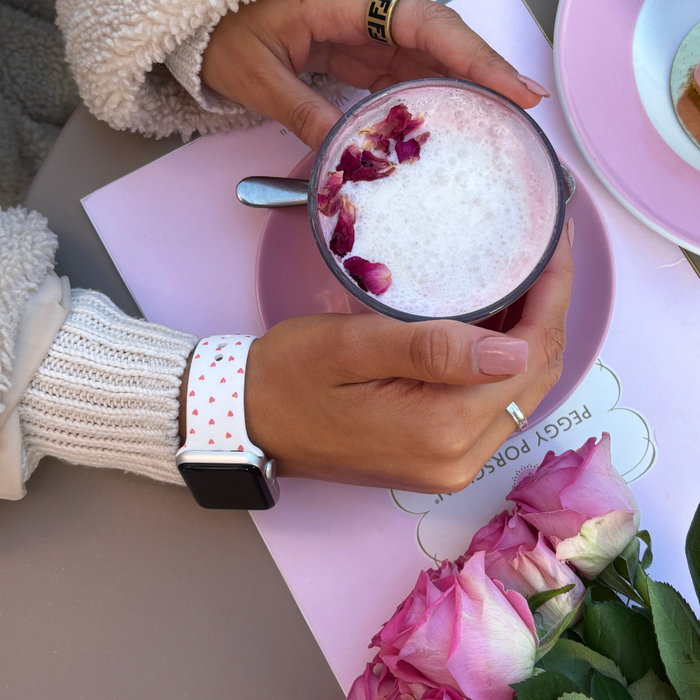 Pink latte with rose petals next to pink roses and a white Mini Hearts Apple Watch strap by Coconut Lane.