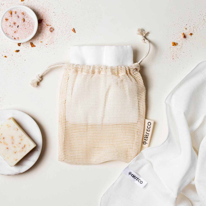 Cotton muslin cloths in drawstring wash bag styled on a surface with bath soap and salts.