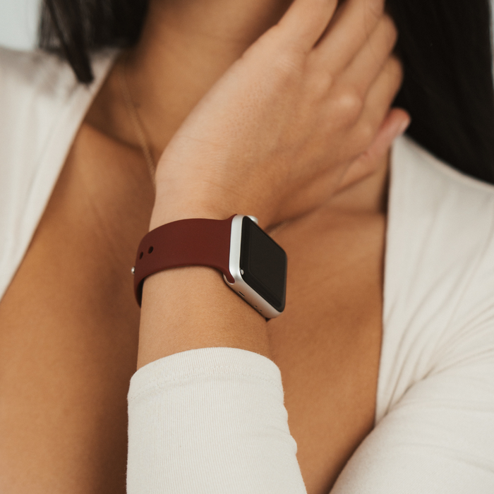 Person in a white top wears a burgundy Coconut Lane NAKD Apple Watch Strap, hand resting near their neck.