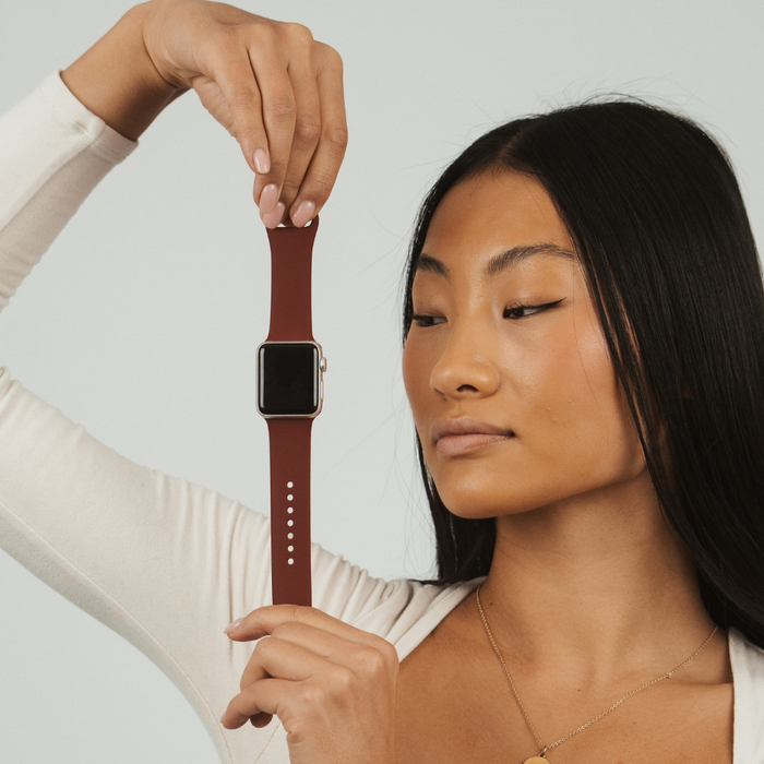 Woman in a white top holds a burgundy Apple Watch strap by Coconut Lane against a plain background.
