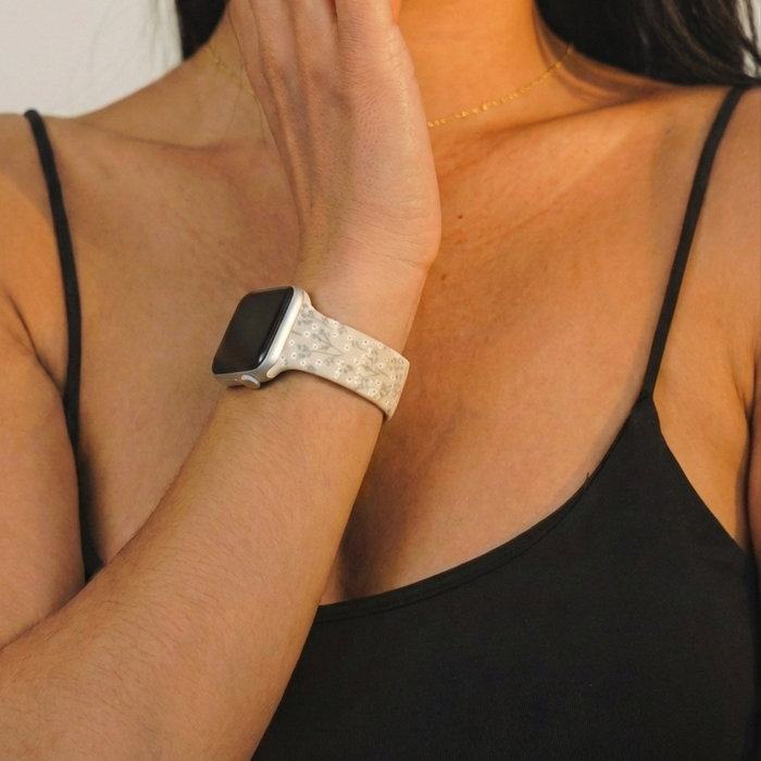 Woman in a black spaghetti strap top wearing a floral nude Apple Watch strap, hand resting on her face.