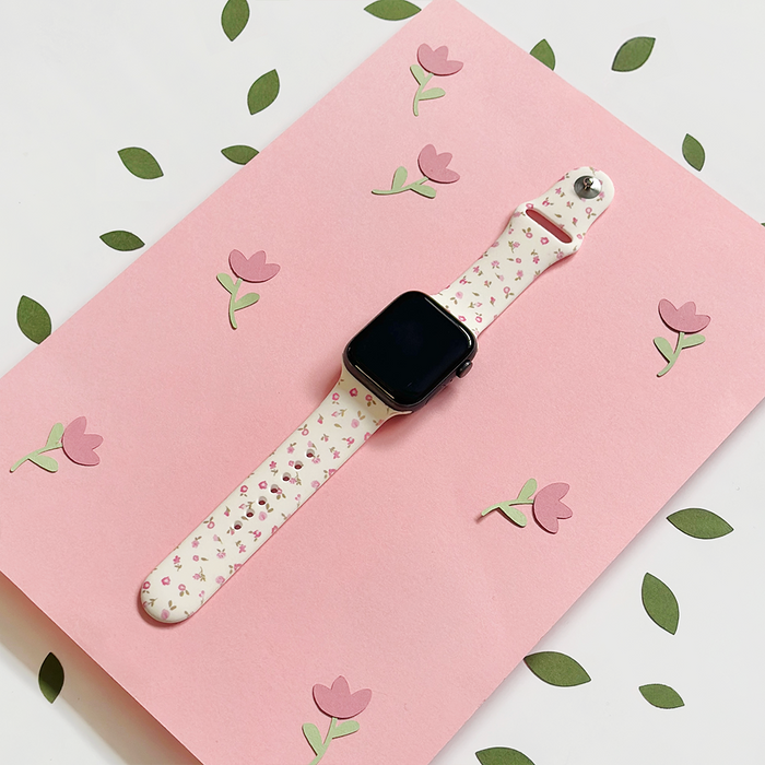 Pink Watercolour Flowers Apple Watch strap with a floral pattern, shown on a pink card with paper flowers.