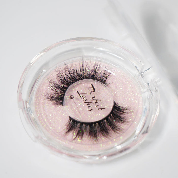 Dramatic false eyelashes in a round, clear case with a pink, glittery background and the Perfect Lashes label for a glamorous look.