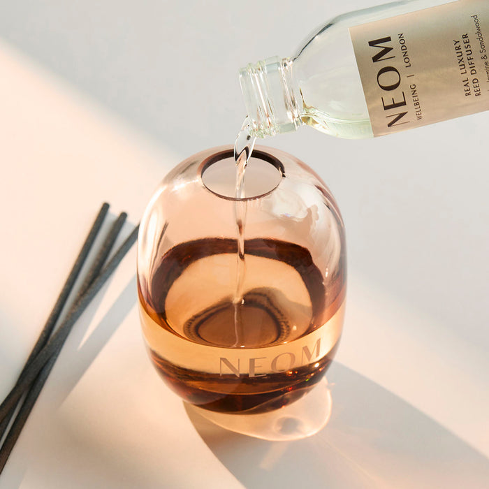 NEOM Real Luxury diffuser refill being poured into glass vessel, reusable luxury home fragrance diffuser