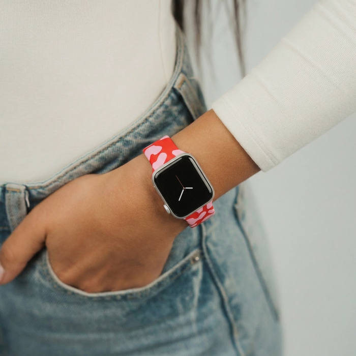 Red and pink leopard print Apple Watch strap on a wrist, hand in jeans pocket, white top visible.