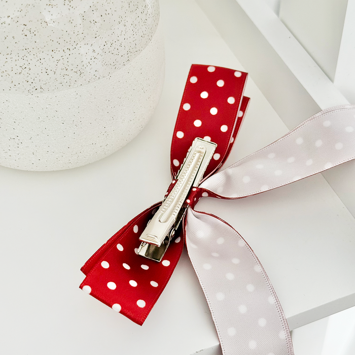 Burgundy polka dot ribbon bow clip on a white surface next to a textured white vase.