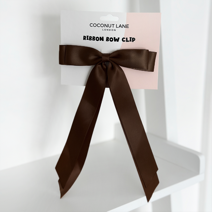 Chocolate satin ribbon bow hair clip with long tails, displayed on a white Coconut Lane branded card.