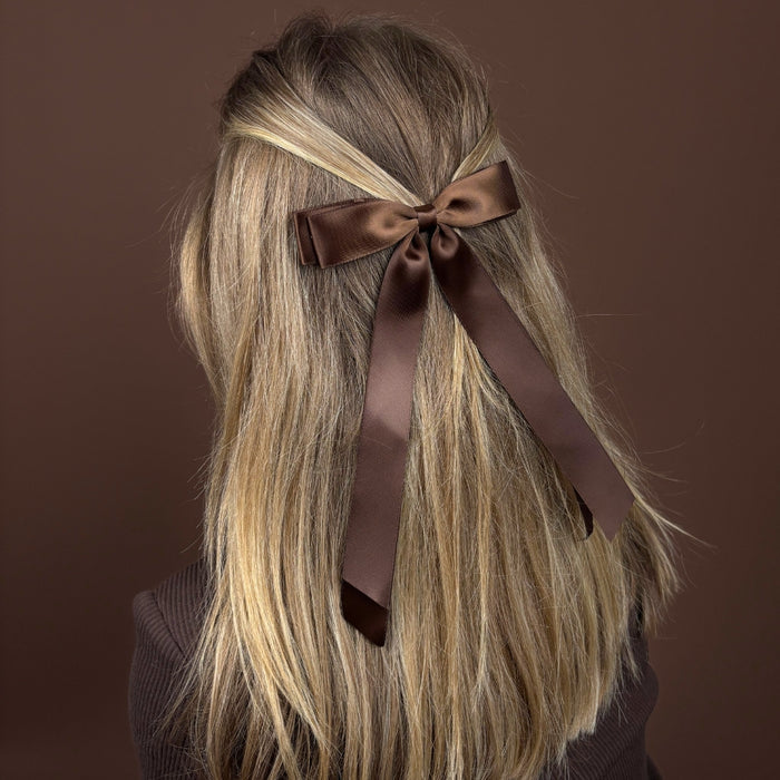 Chocolate satin ribbon bow clip securing a half-up style in long blonde hair, as the woman faces away.