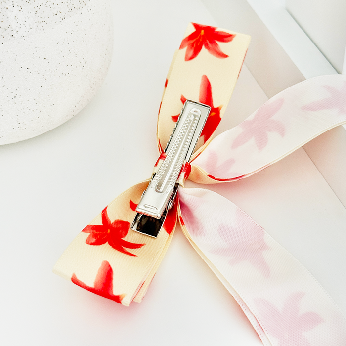 Satin ribbon bow clip with a metal clasp displayed on a white surface.