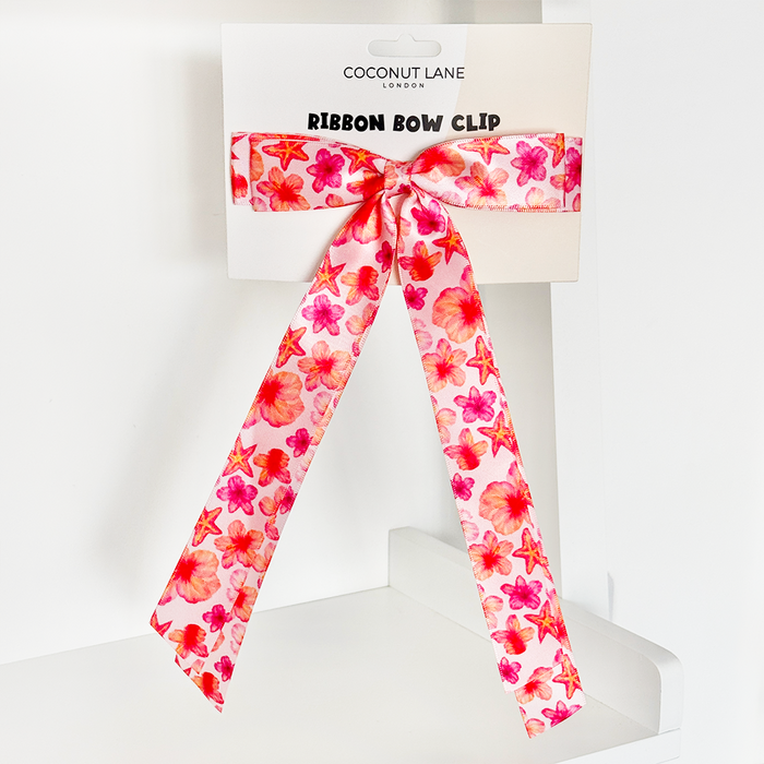 Pink ribbon bow hair clip with hibiscus print displayed on Coconut Lane branded card.