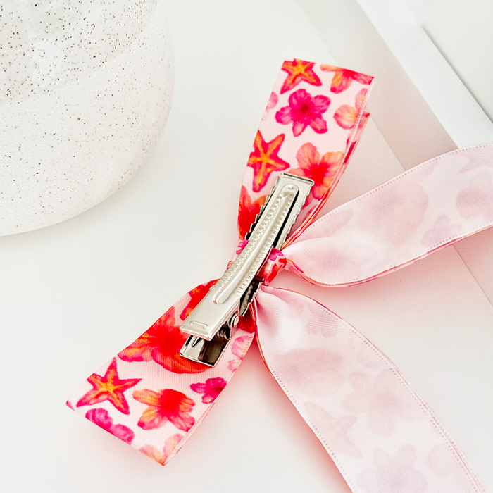 Pink hibiscus-patterned ribbon bow clip on a white surface next to a speckled container.