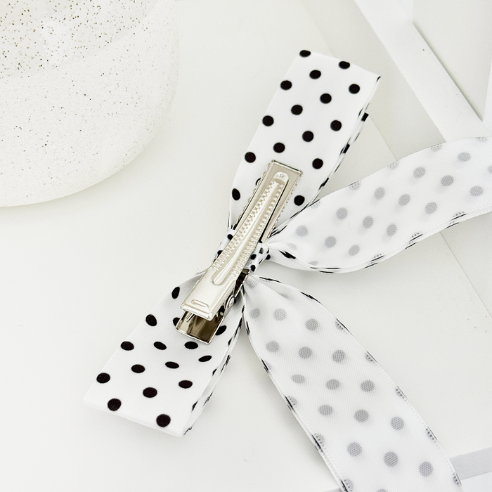 White polka dot ribbon bow hair clip from Coconut Lane beside a textured white container.