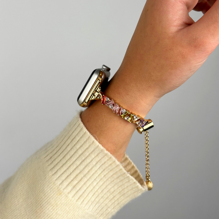 Gold Coconut Lane Riviera Crystals Apple Watch strap with a chain band and multicolored gemstones on a wrist.