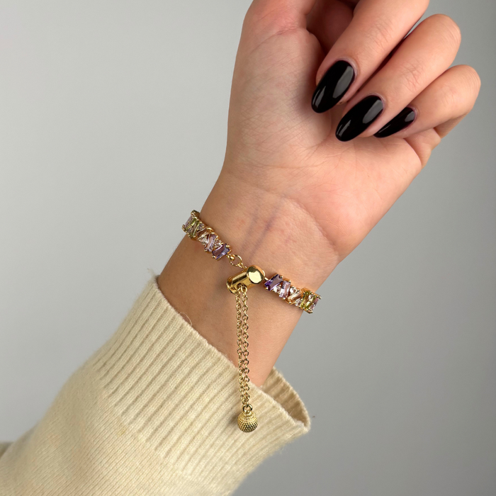 Gold Apple Watch strap with pink crystal accents and adjustable clasp on a hand with black nails.
