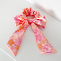 Pink satin scrunchie with bow, featuring orange and pink floral patterns.