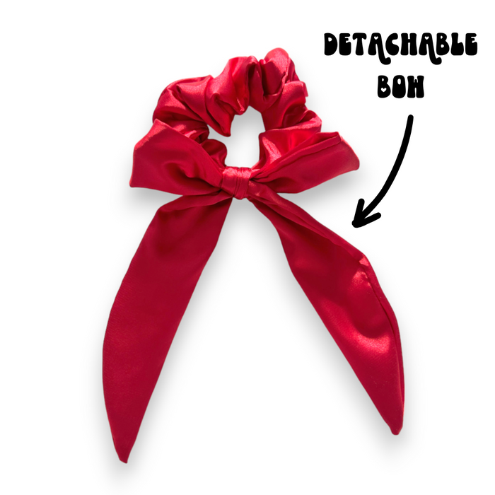 Rose red satin scrunchie with detachable bow, shown with a black arrow and text label.