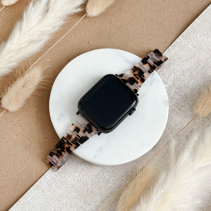 Slim Luxe Ivory Tort Apple Watch strap with a marble pattern, displayed on marble surface near dried pampas grass.
