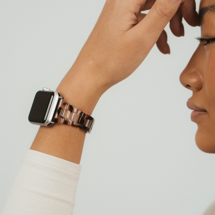 Coconut Lane Slim Luxe Ivory Tort Apple Watch strap worn on wrist, hand raised near face, plain background.
