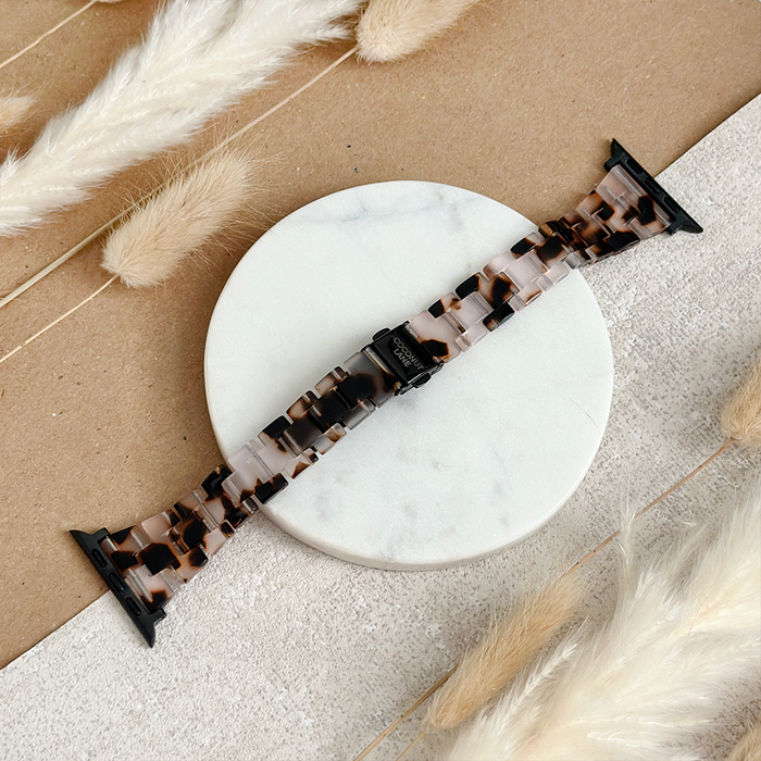 Slim Luxe Ivory Tort Apple Watch strap by Coconut Lane on a marble surface with soft pampas grass nearby.