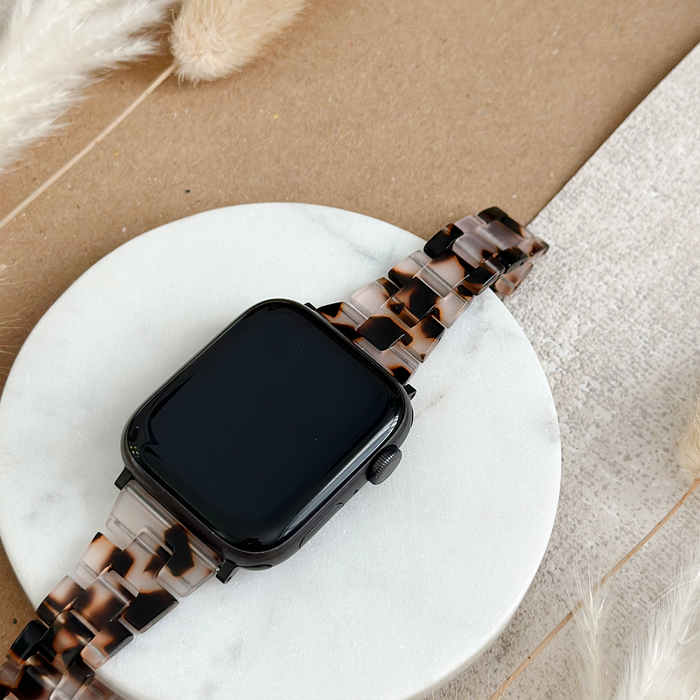 Ivory tortoiseshell Apple Watch strap with a slim, glossy finish shown on a round white surface with beige accents nearby.
