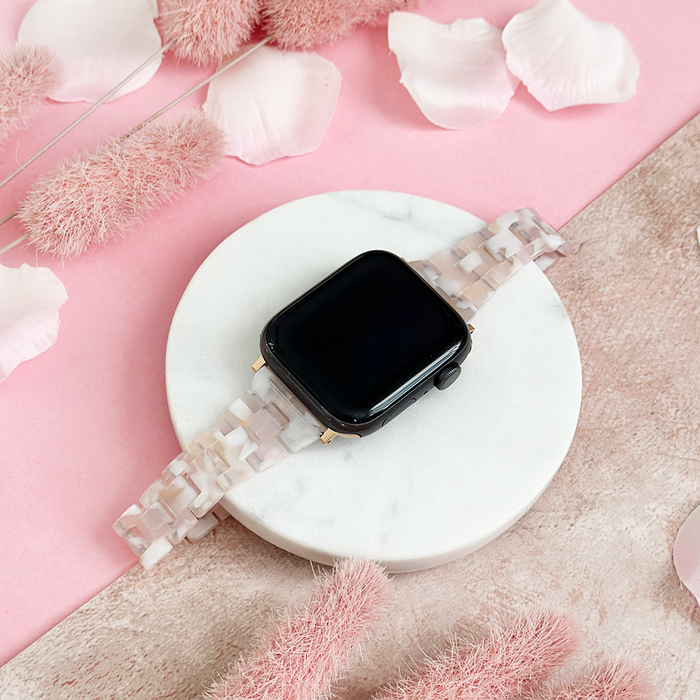 Slim Luxe Rose Apple Watch strap by Coconut Lane on a white dish with pink petals and dried flowers.