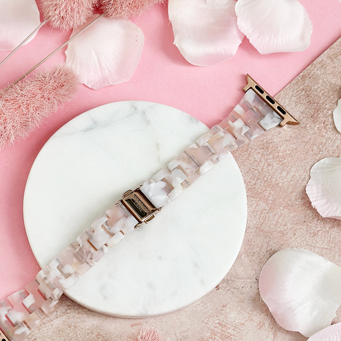 Slim Luxe Rose Apple Watch strap with a pink and white marble pattern, shown on a tray with flower petals.