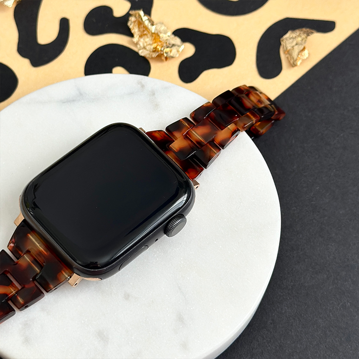 Slim tortoiseshell Apple Watch strap with gold accents on white marble background.