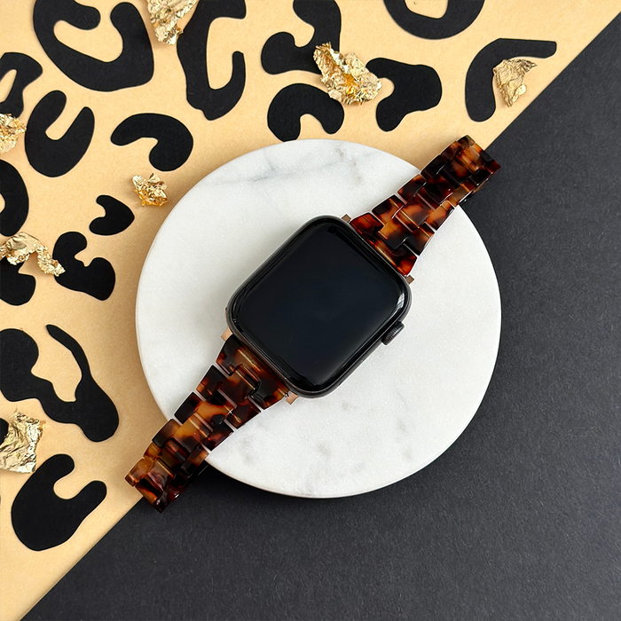 Slim Luxe Tortoiseshell Apple Watch strap on a marble tray with gold flakes, animal print background.