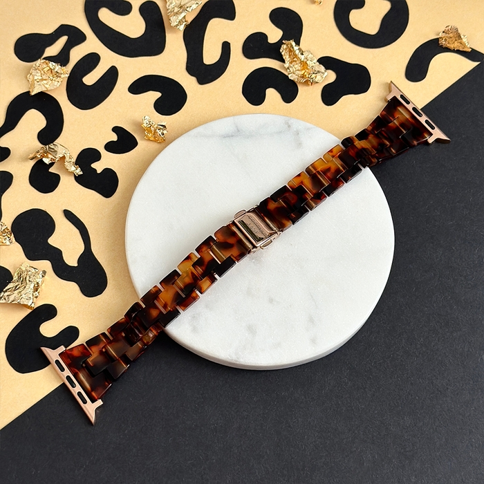 Slim luxe tortoiseshell Apple Watch strap by Coconut Lane on white marble with a black and gold animal print background.