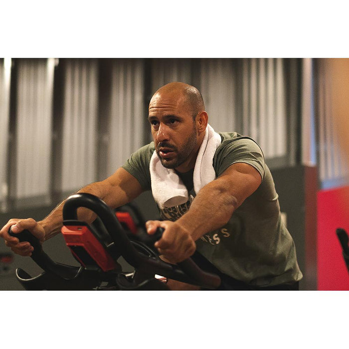 A person working out on a Peloton with a white Spa and Workout towel around his neck.