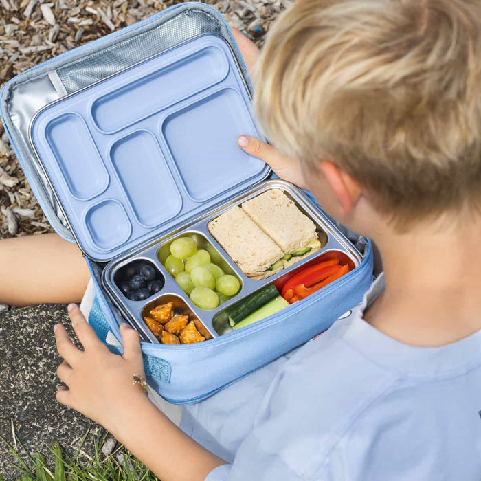 Child sitting in the grass with his lunch bag containing the Ever Eco stainless steel bento lunch box with snacks & sandwiches in each of the compartments.