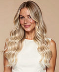 Woman with long, wavy blonde hair wearing Irresistible Me tape in hair extensions against a beige background