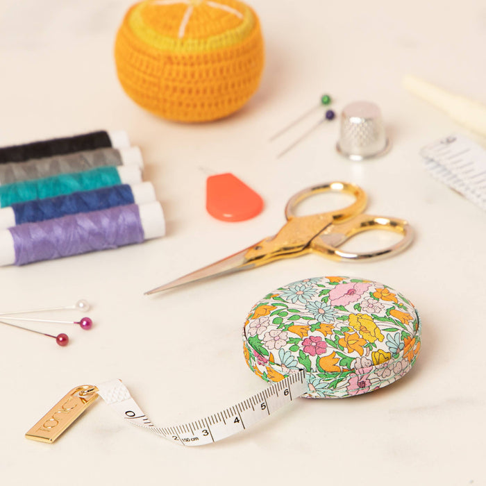 Floral tape measure on a light surface with sewing tools including scissors and thread.