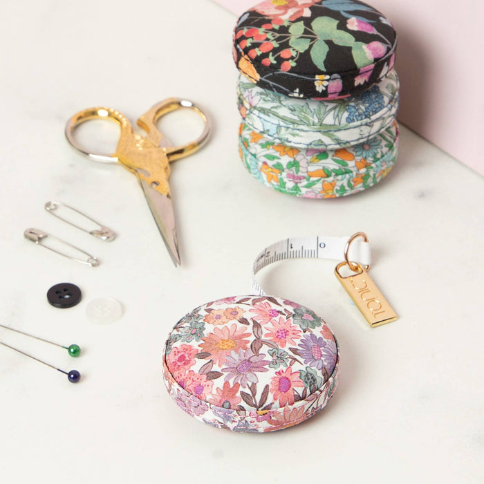 Set of sewing tools including scissors, pins, buttons, and a tape measure with floral cases on a white surface.
