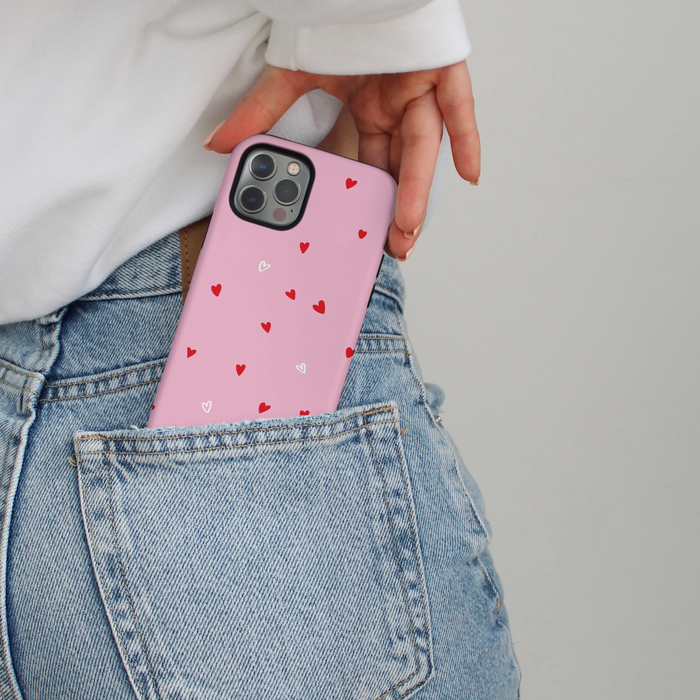 Pink Coconut Lane Tough MagSafe® phone case with red heart pattern partially tucked into classic blue jeans.