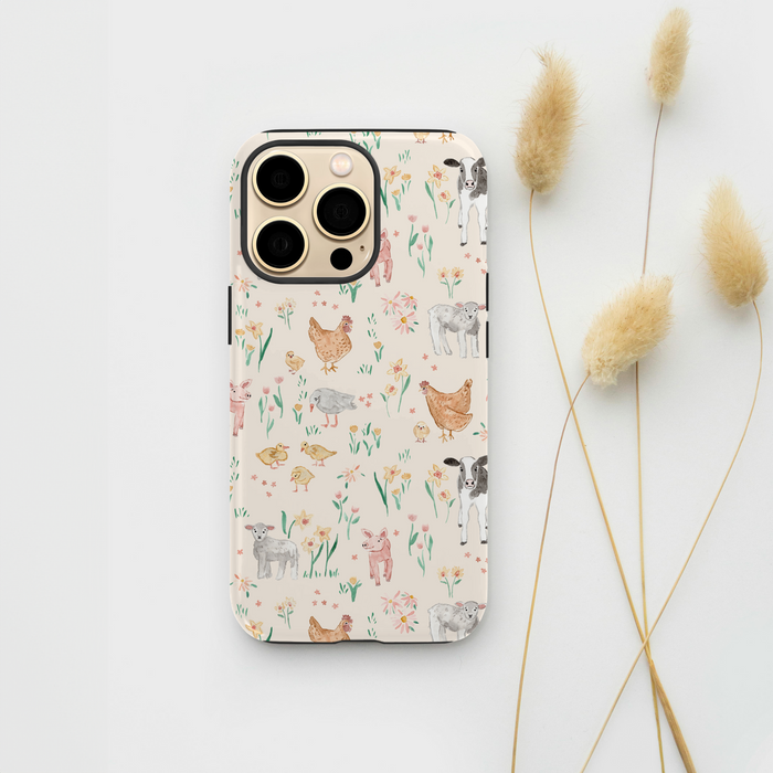 Coconut Lane Farmyard Friends phone case with animal and flower pattern, shown next to beige dried grasses on white background.