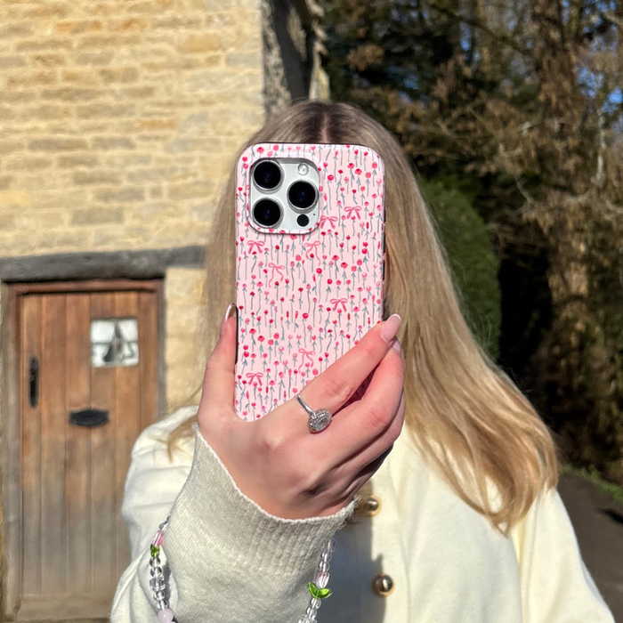 Cream-coated person holds a Coconut Lane Peony Bow tough phone case with pink bow pattern, obscuring their face.