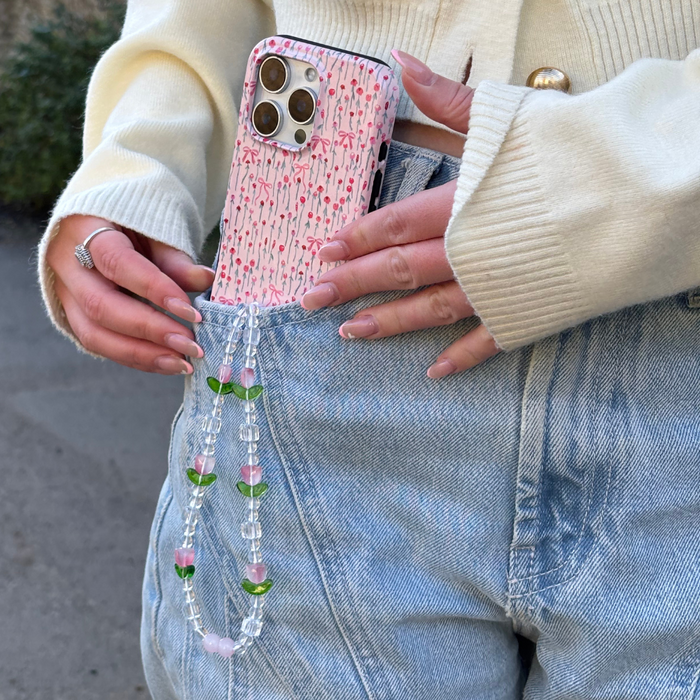 A hand slides a Coconut Lane Tough Phone Case with a pink peony bow design into the pocket of light blue jeans.