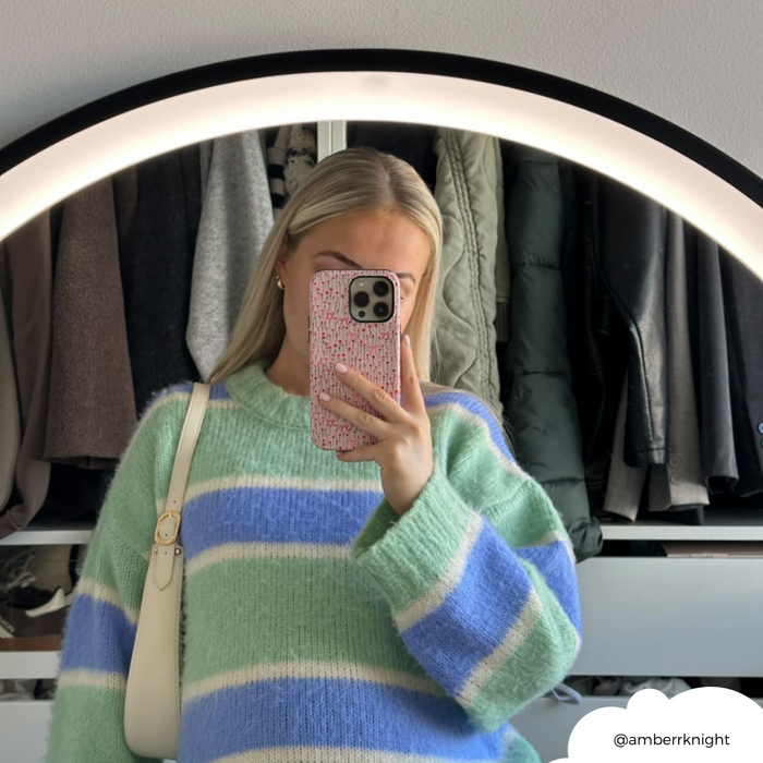 Woman in striped sweater holds Coconut Lane Tough Phone Case with pink peony bow pattern, taking a mirror selfie.