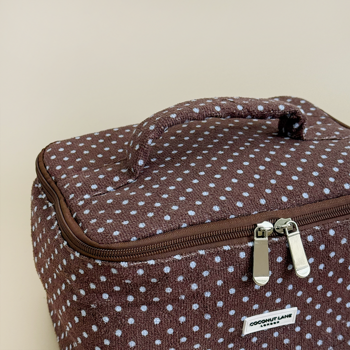 Brown and blue polka dot vanity case with handle and zipper, displayed on a beige background.