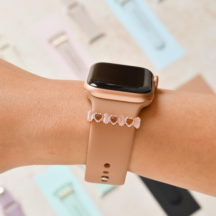 Rose gold Coconut Lane smartwatch with a beige band and a rose gold crystal heart charm on the strap, worn on wrist.