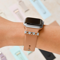 Apple Watch with a tan silicone band, silver crystal heart charm, and a matching silver heart bracelet.